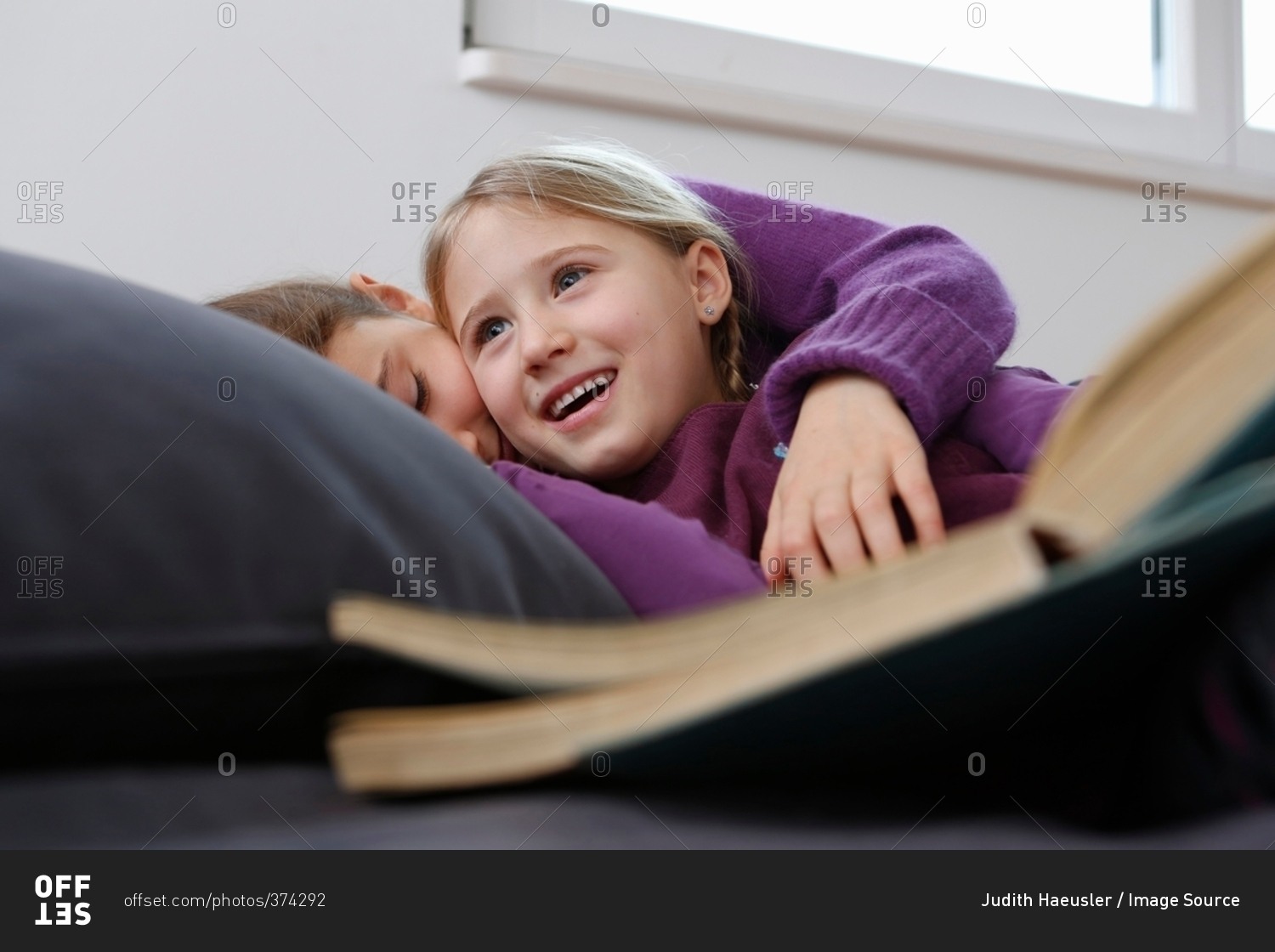 Surface level view of girl lying down on sofa with book, hugging and smiling