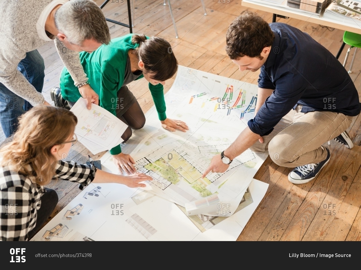 High angle view of architects discussing blueprints on wooden floor