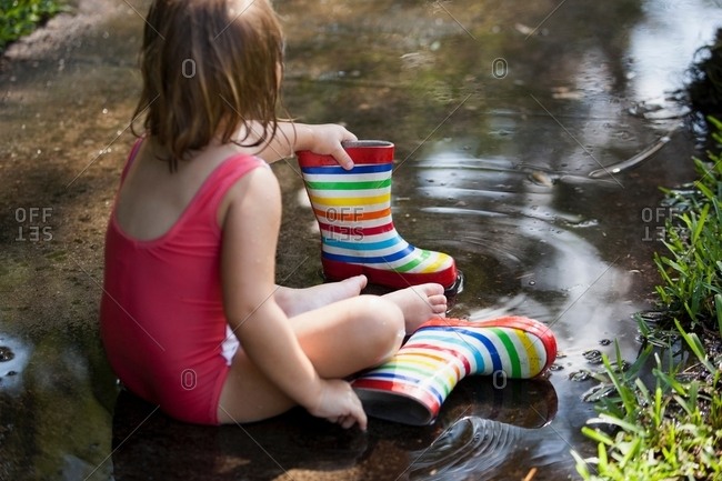 Child in wellies sitting in puddle of water