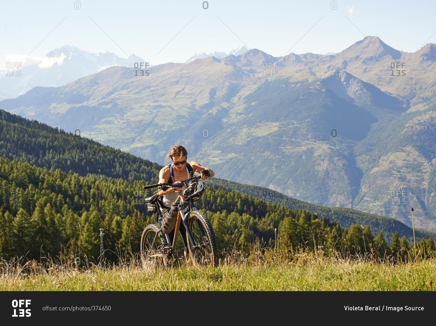 Female mountain biker pushing mountain bike uphill in landscape, Aosta Valley, Aosta, Italy