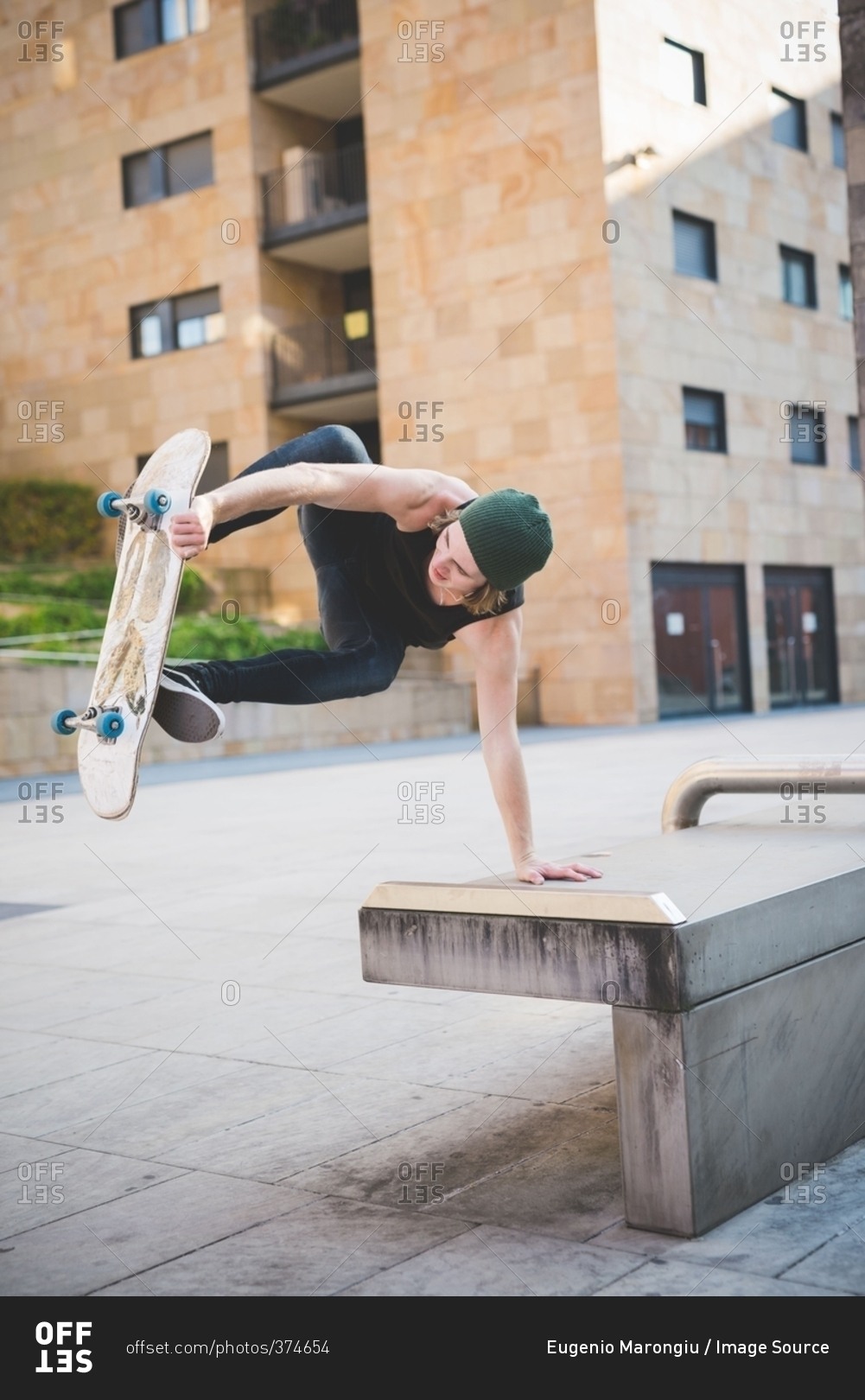 Young male skateboarder doing balance skateboard trick on urban concourse seat
