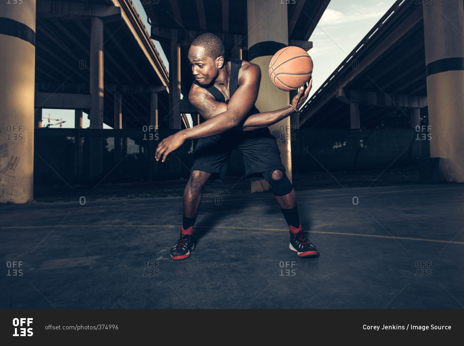 Young man bending forward balancing basketball on hand, looking away