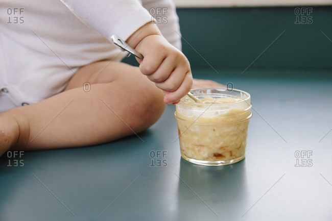 Baby holding a spoon in a jar of homemade baby food