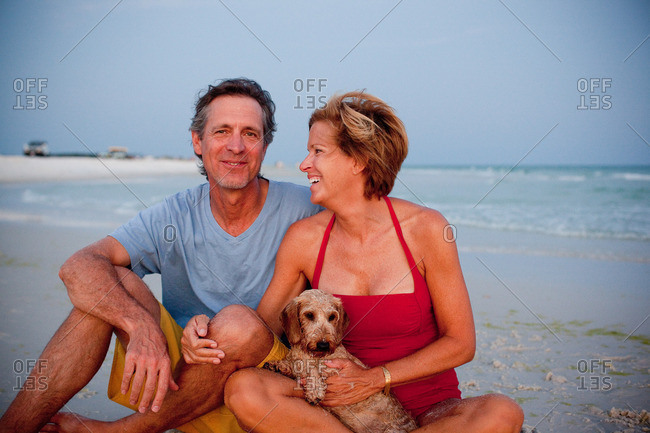 Couple sitting with their dog on a sandy beach