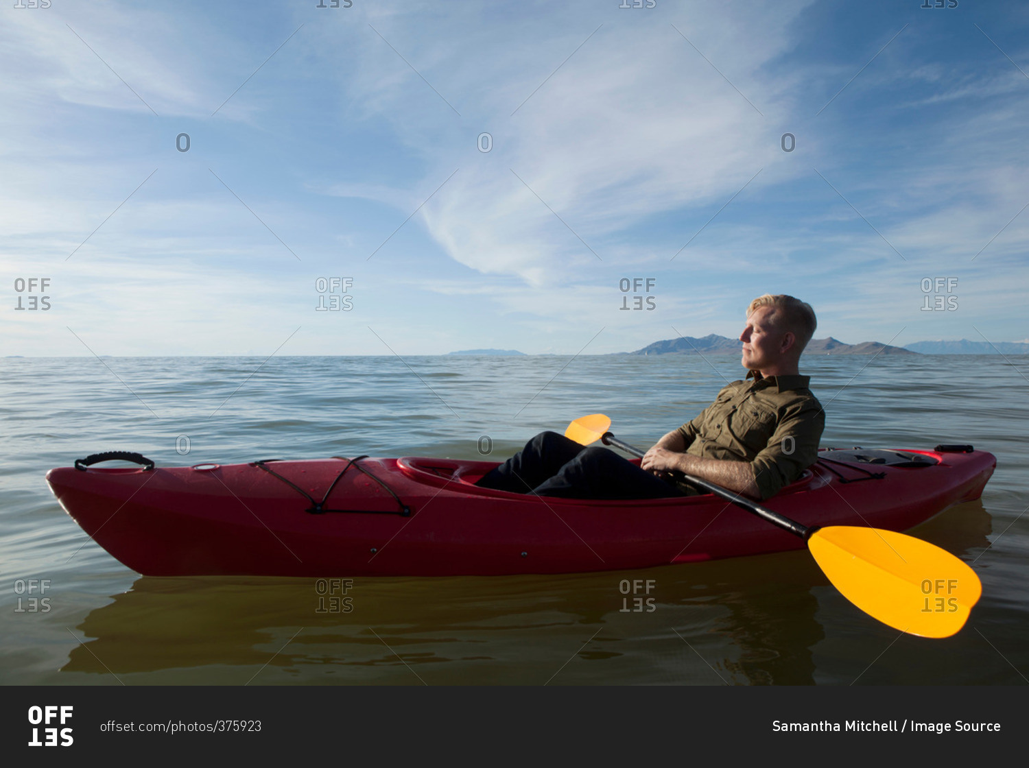 Side view of young man in kayak on water holding paddles, eyes closed, Great Salt Lake, Utah, USA