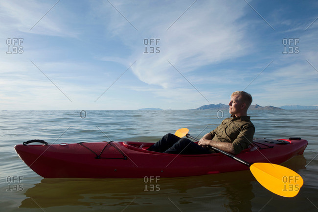 Side view of young man in kayak on water holding paddles, eyes closed, Great Salt Lake, Utah, USA
