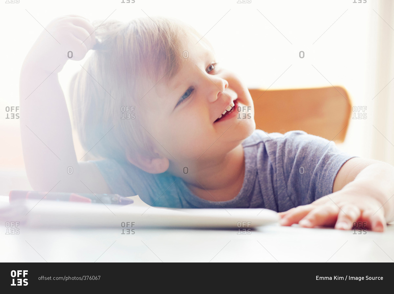Boy sitting at table scratching head, looking away smiling