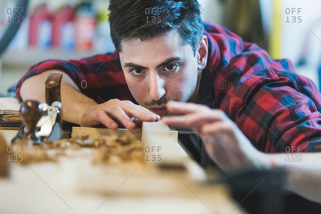 Young man using wood plane to smooth wood object
