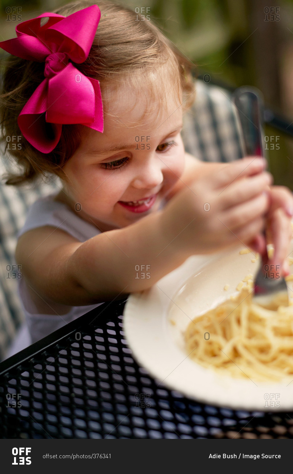 High angle view of girl with pink hair bow sitting at garden eating spaghetti