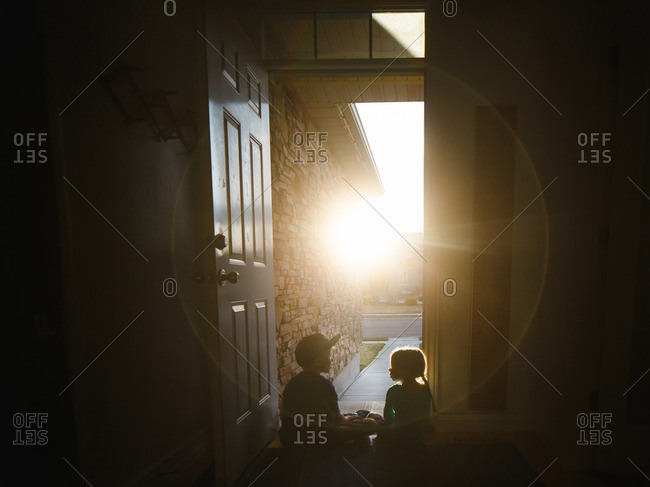 Two children sitting together at the front door of their home at sunset