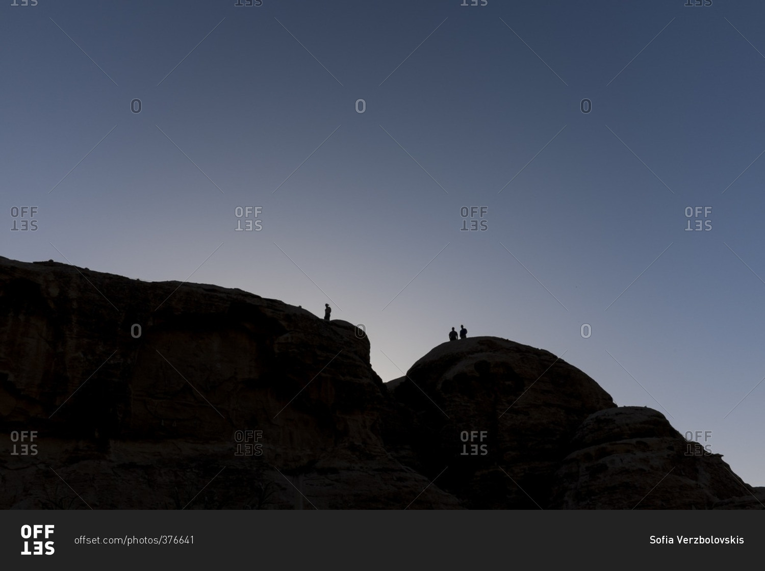 Silhouettes of people walking on top of desert cliffs at sunset