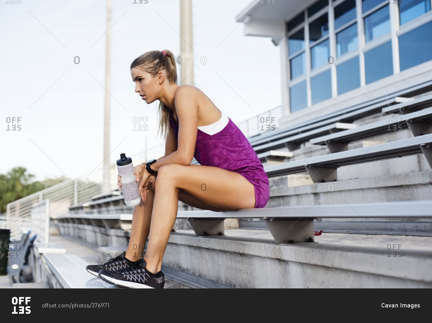 Side view of sporty woman sitting on bleachers at stadium