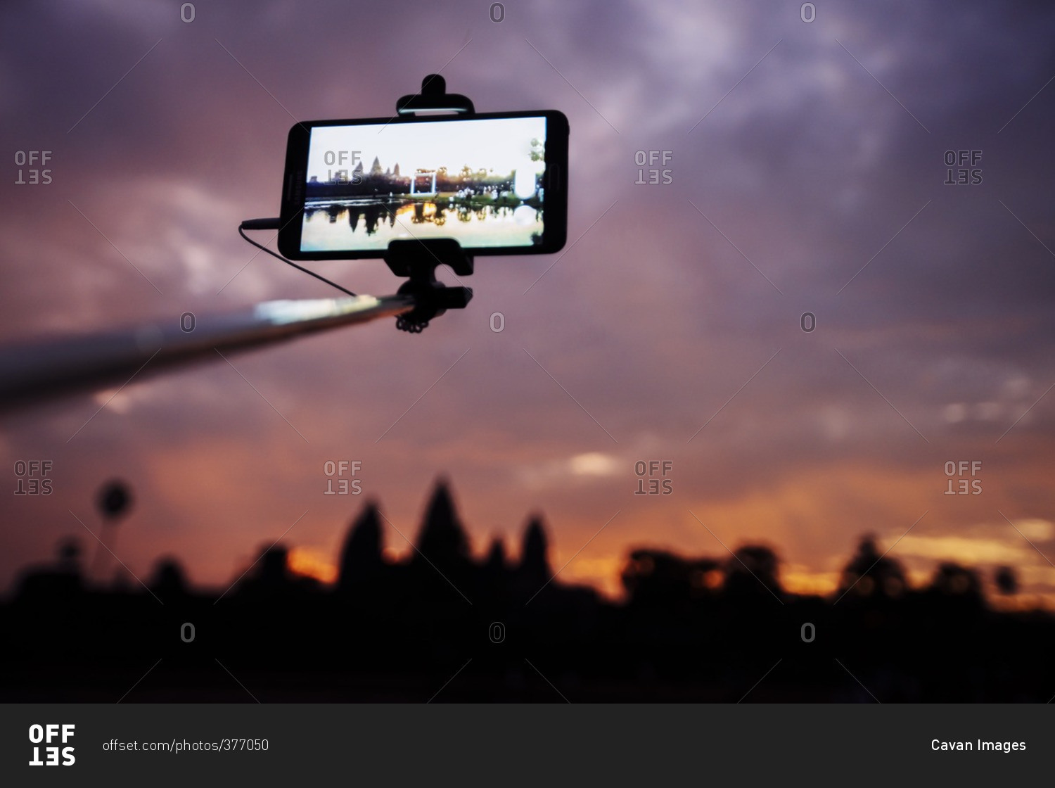 Low angle view of smart phone attached to monopod photographing silhouette Angkor Wat temple during sunset