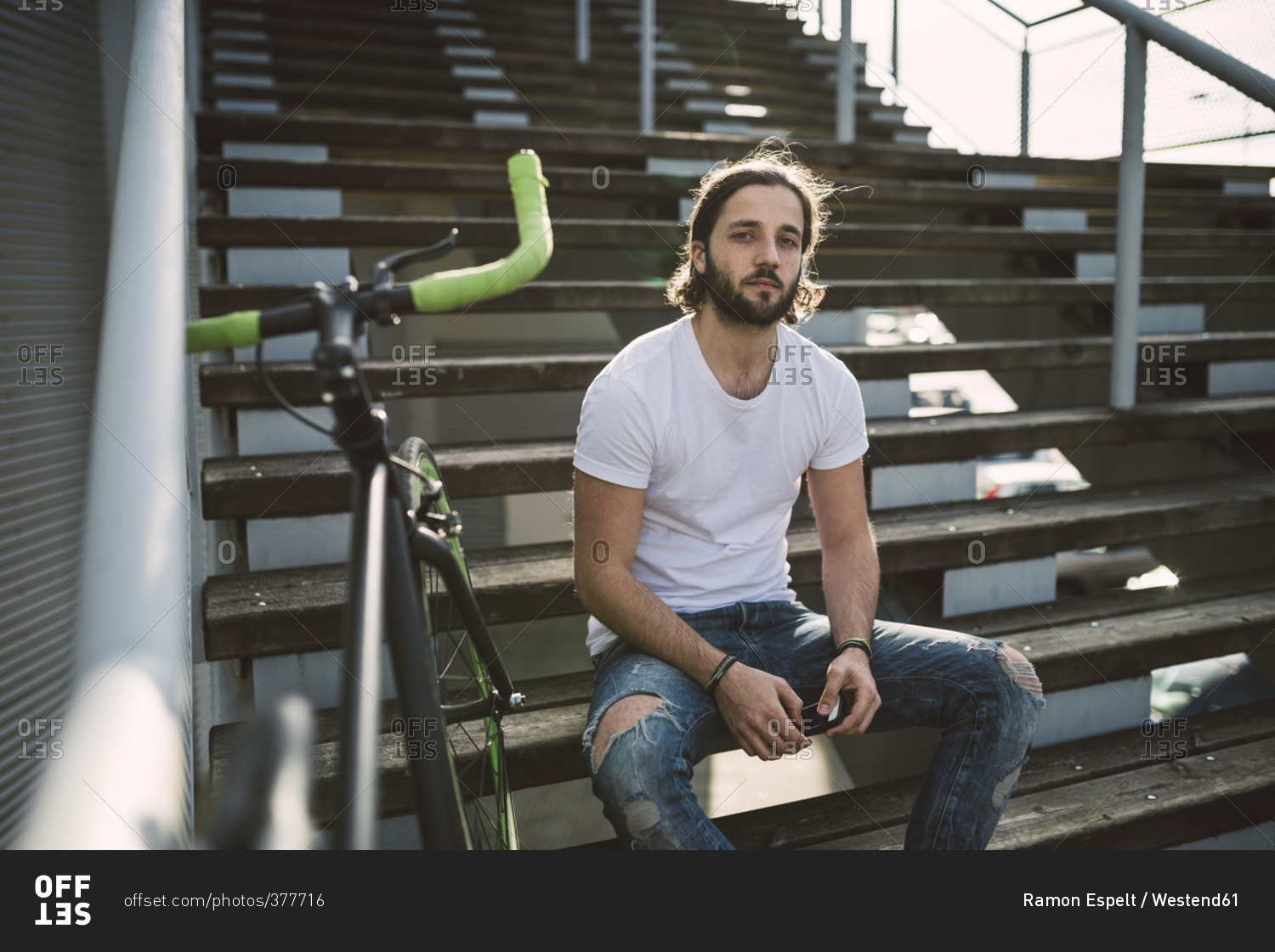 Young man sitting on stairs next to bike