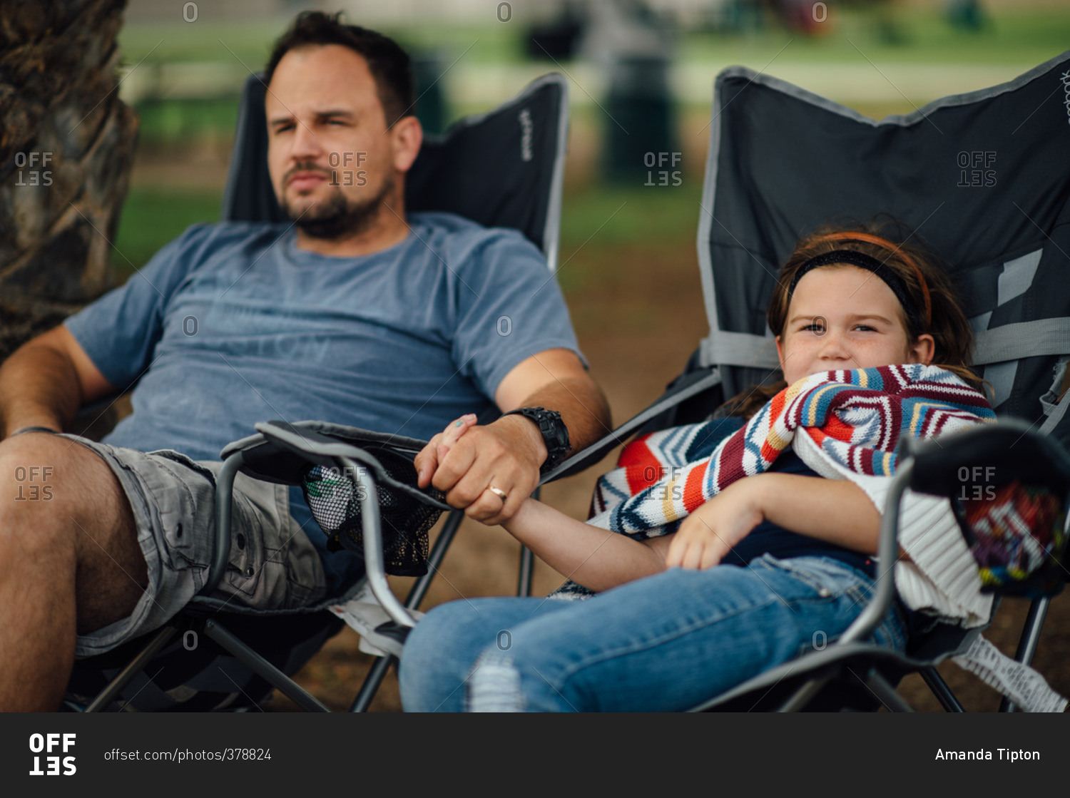 Father and daughter sitting in lawn chairs holding hands