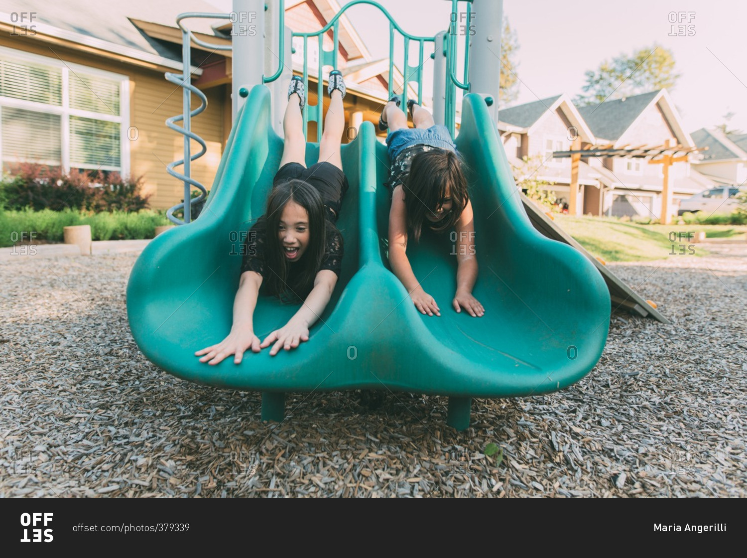 Two young girls sliding headfirst down slide stock photo - OFFSET