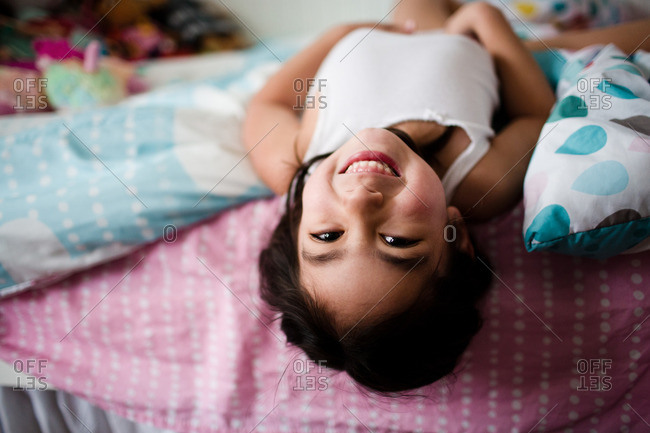 Smiling young girl hanging upside down on bed