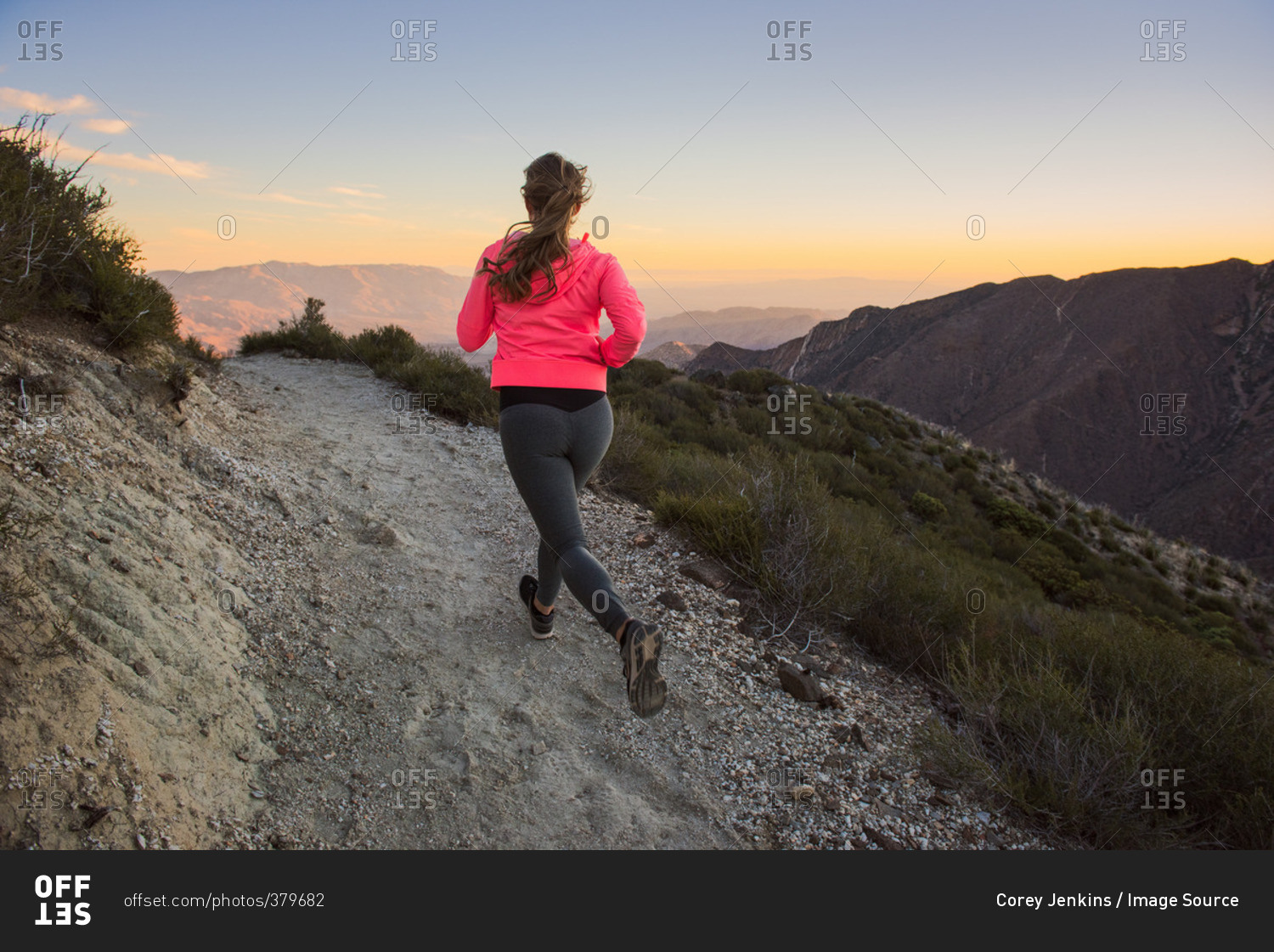 Rear view of young woman trail running up dirt track at dusk on Pacific Crest Trail, Pine Valley, California, USA