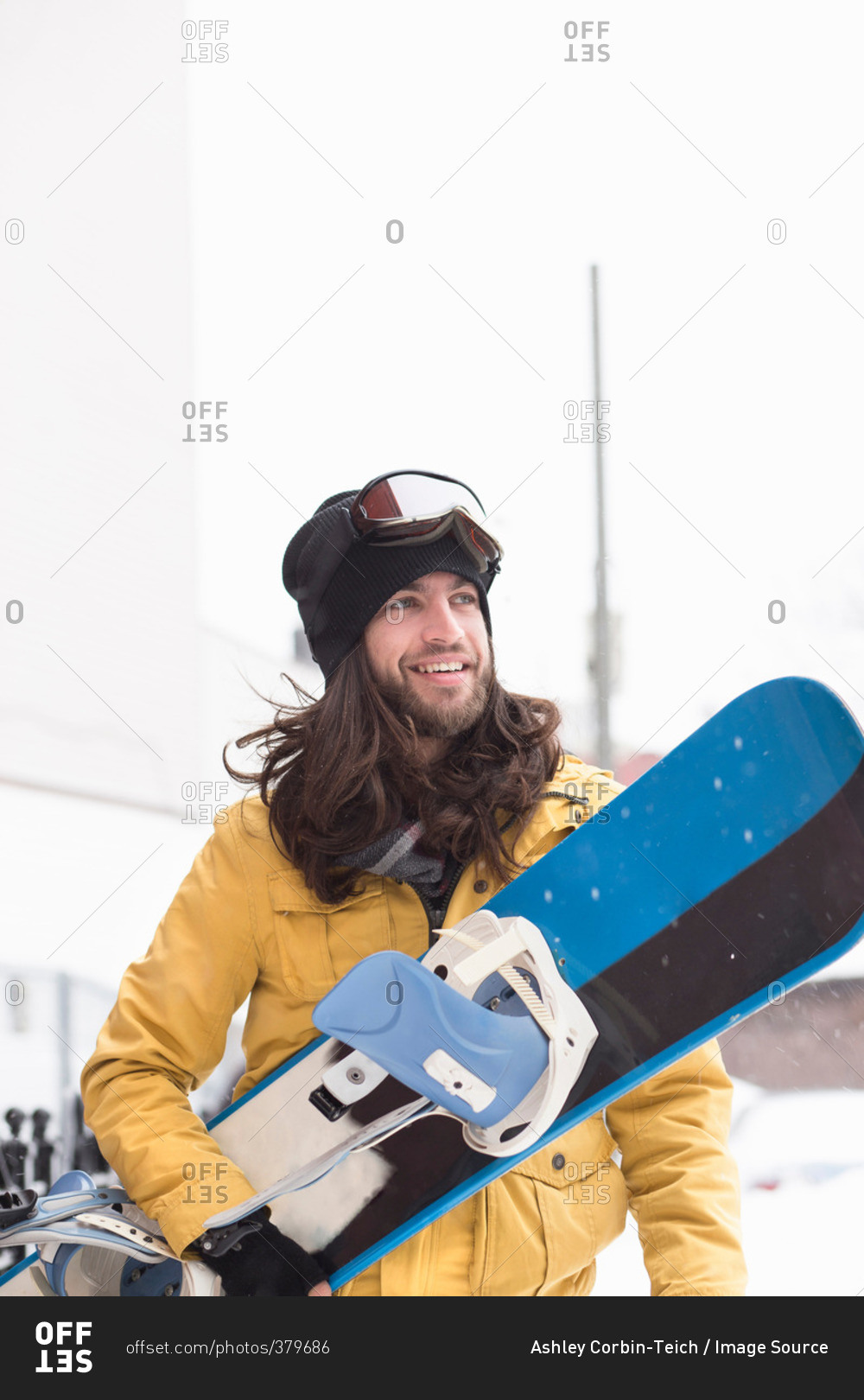 Smiling male snowboarder carrying snowboard in street