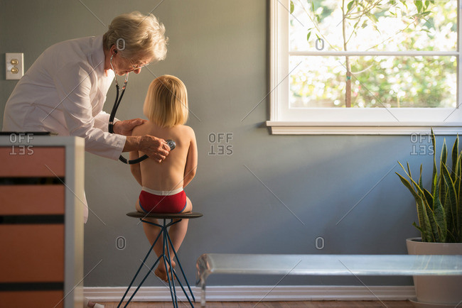 Female doctor listening to stethoscope on boys back in doctors office