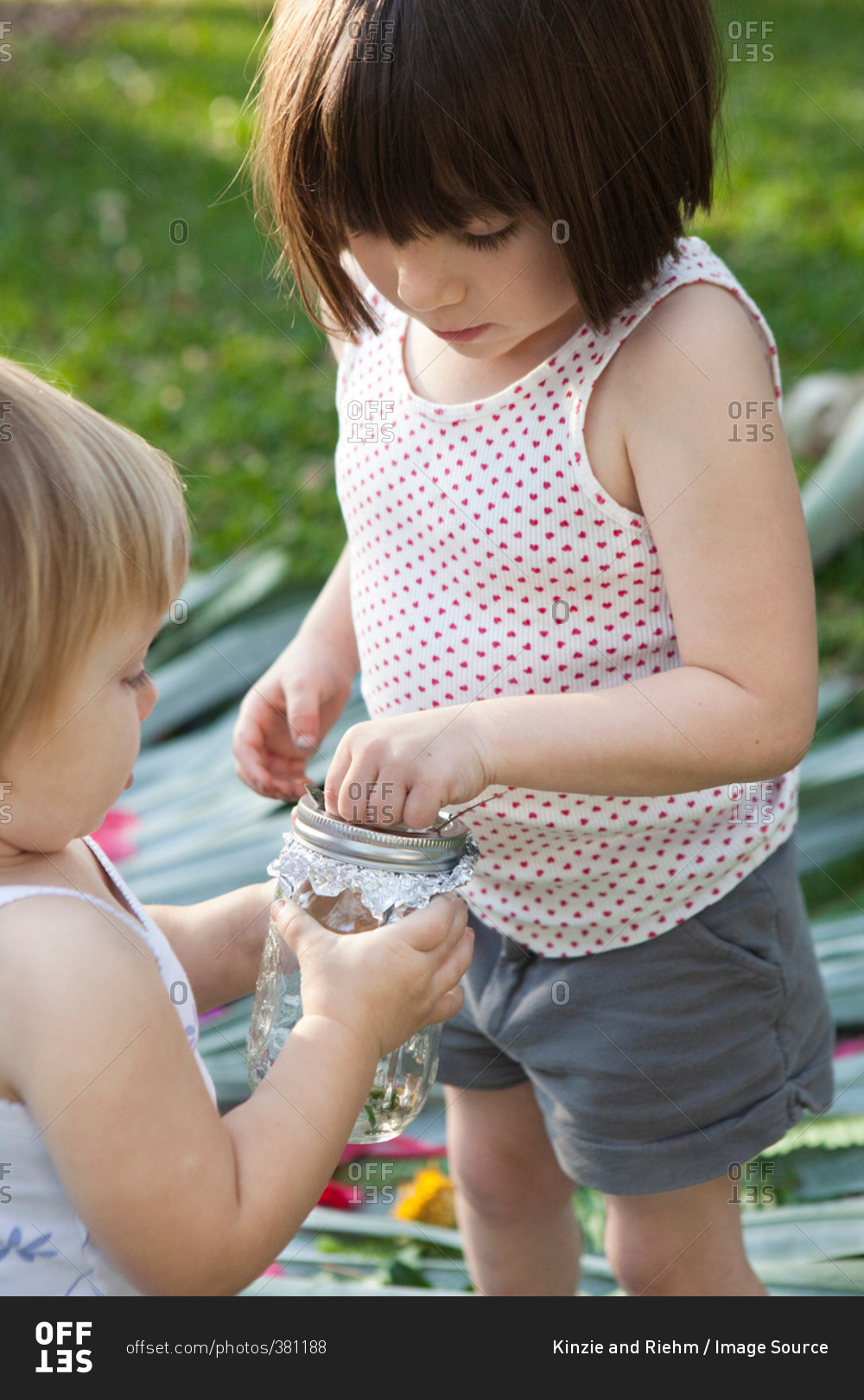 Girl and toddler sister holding jar with green anole lizard in garden