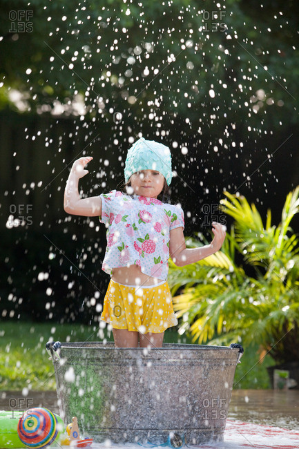 Girl standing in bubble bath in garden splashing soap bubbles
