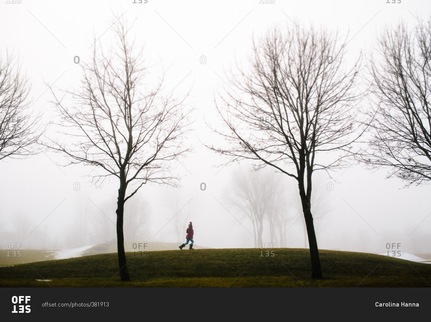 Girl running through a field with her arms outstretched on a cold, foggy day