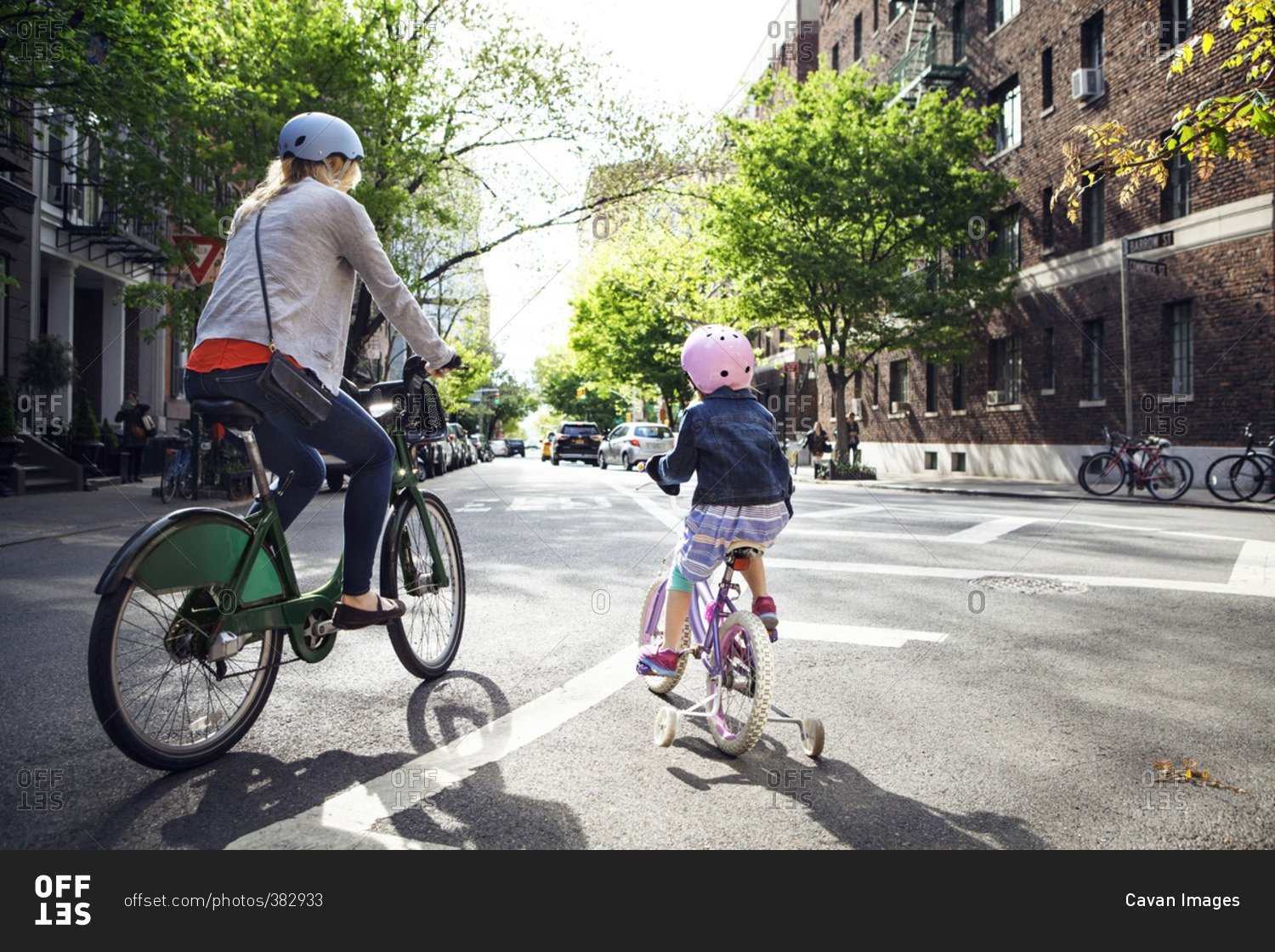 Rear view of mother and daughter riding bicycles on street