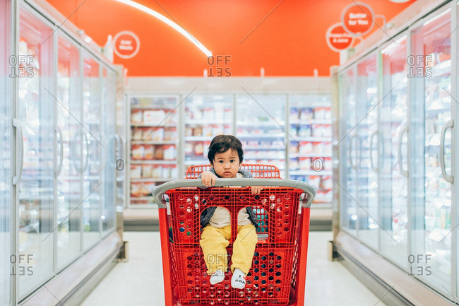 Asian baby sitting in a red shopping cart