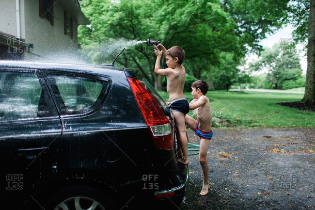 Two boys in underwear spraying a car with water