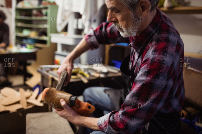 Profile view of cobbler stapling a shoe in his workshop