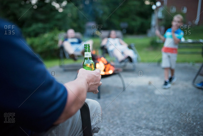 Man Holding A Beer And Sitting With Family And Friends Near An