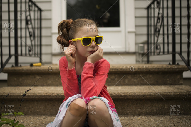 Little girl in yellow sunglasses sitting on a cement stoop