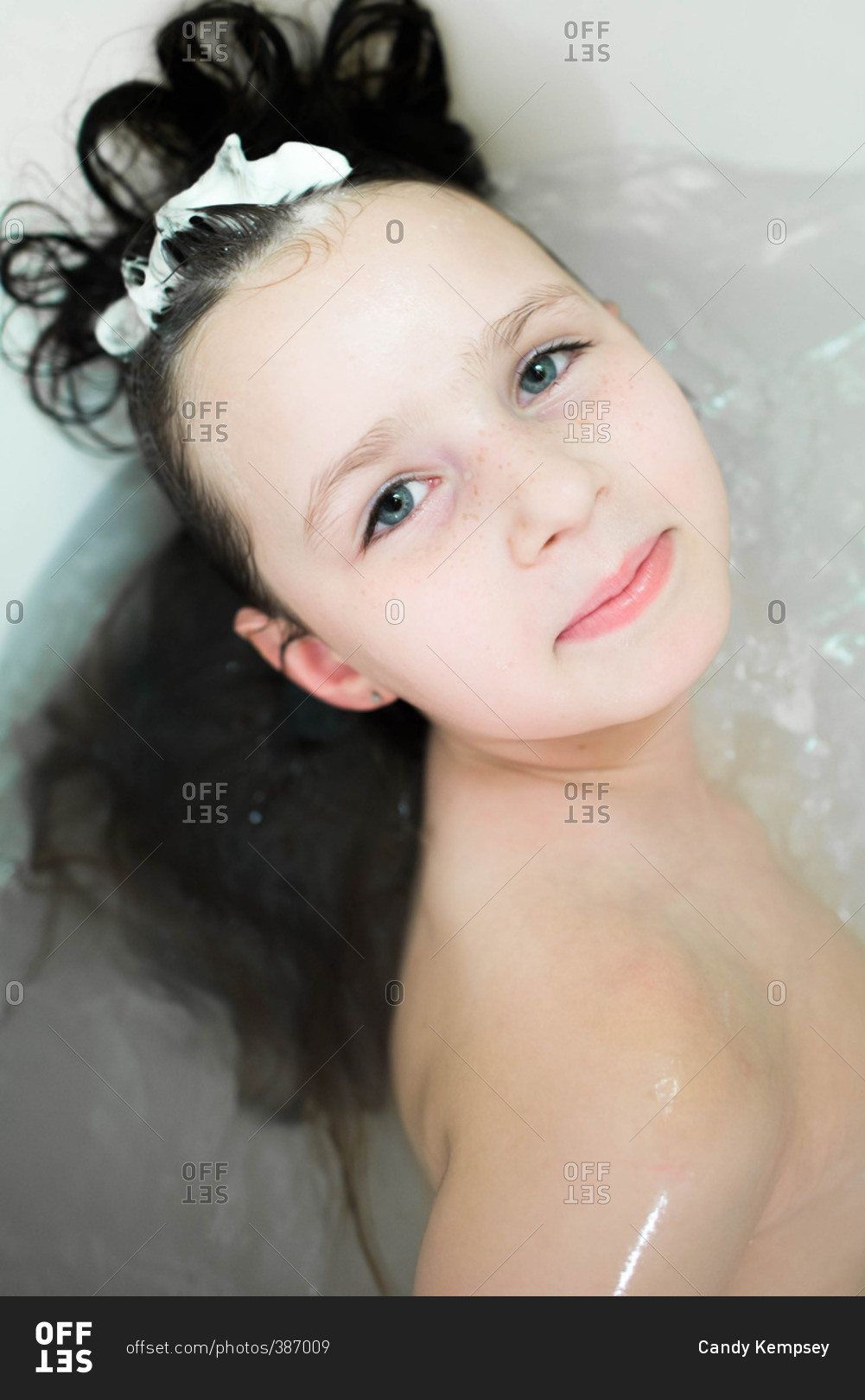 Little girl washing her hair in a bath with foam on her head stock