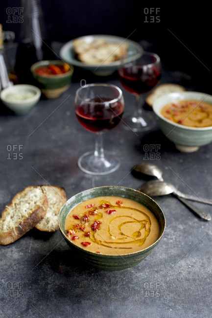 Sun-dried Tomato Pesto White Bean Soup topped with sun-dried tomato and chili oil in a ceramic bowl with Asiago Crostini and red wine.  On a black/grey background.  Photographed from front view.