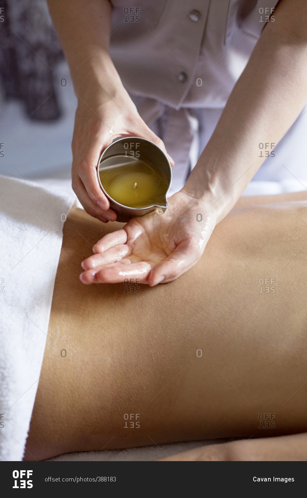 Midsection of therapist pouring essential oil on woman's back in spa