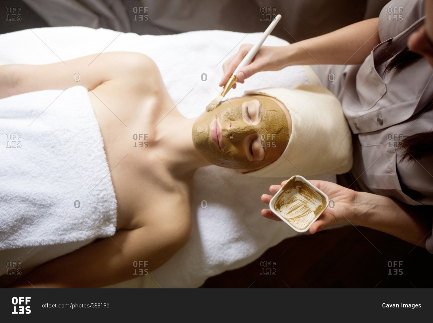 Overhead view of female therapist applying facial mask on woman's face in spa