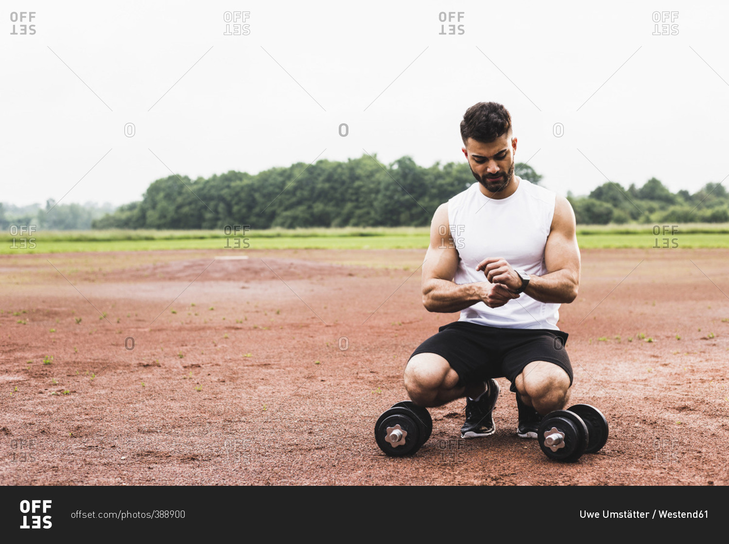 Athlete crouching with dumbbells on sports field