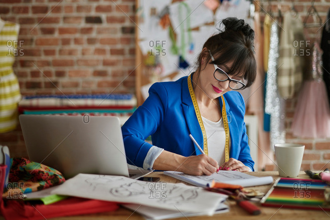 Woman in design studio sitting at desk sketching fashion design