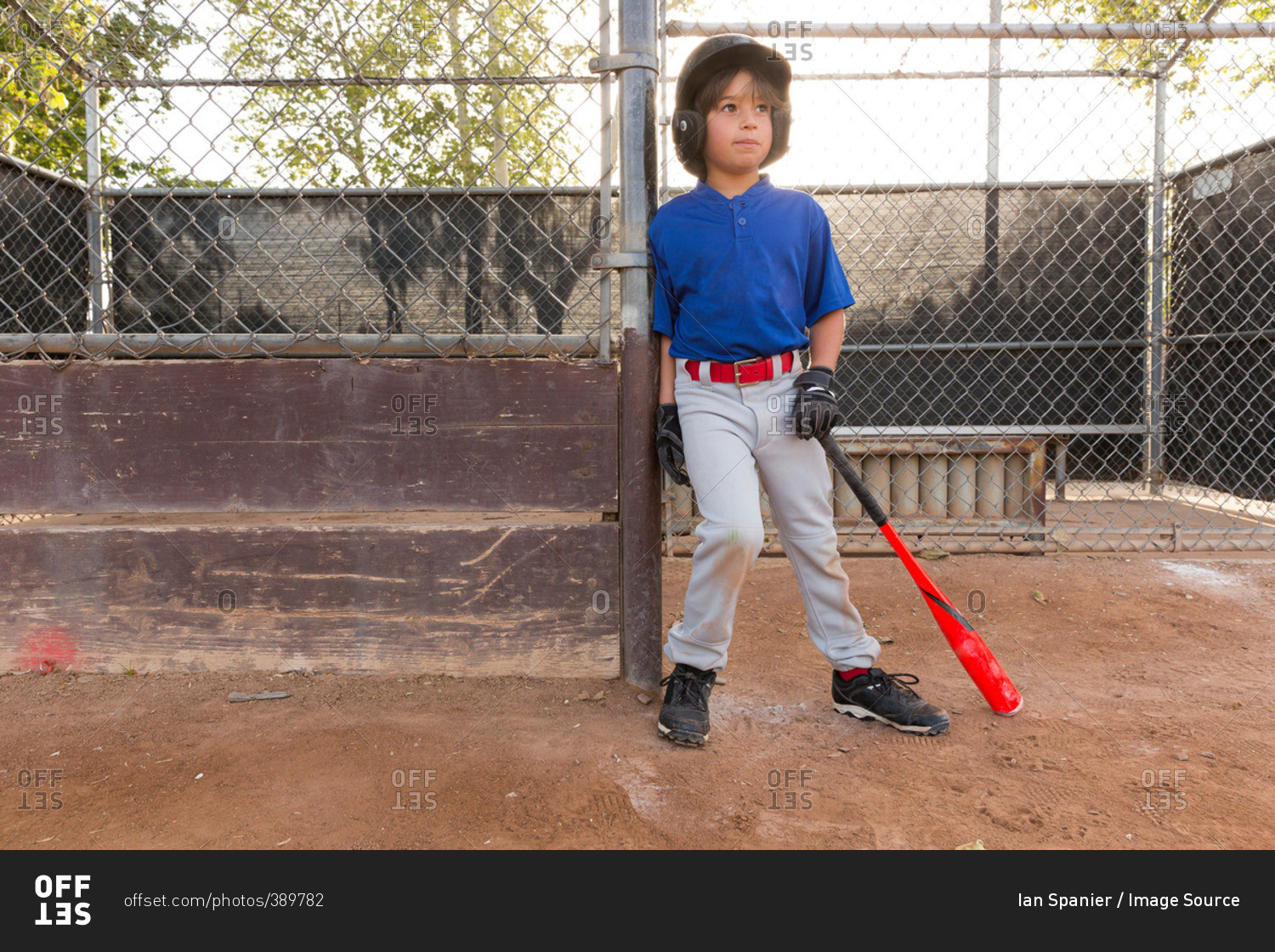 Boy leaning against fence with baseball bat at practice on baseball field