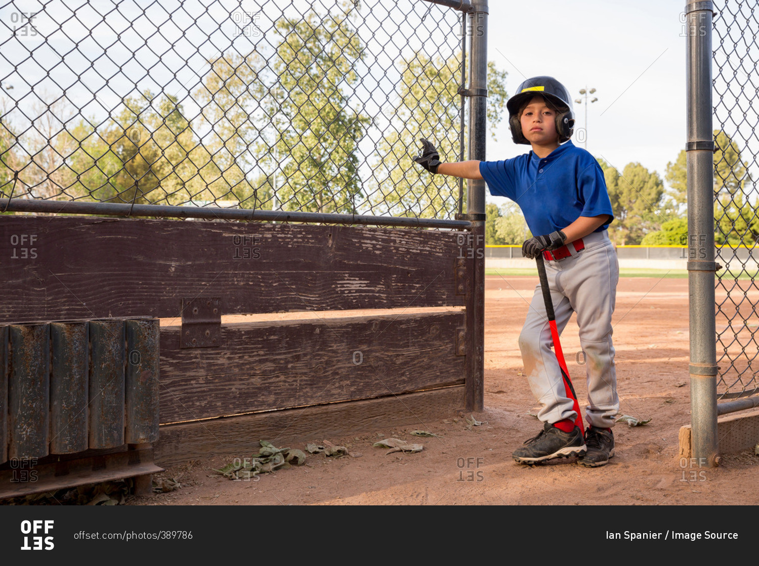 Portrait of boy with baseball bat leaning against fence at baseball practice
