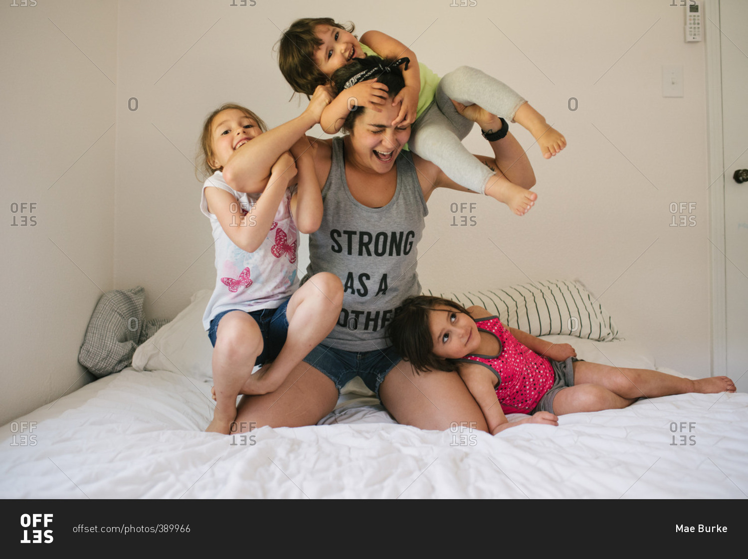 Mom wrestling with her three daughters on a bed