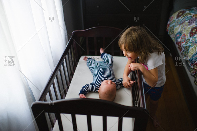 Big Sister Playing With Her Baby Brother In A Crib Stock Photo