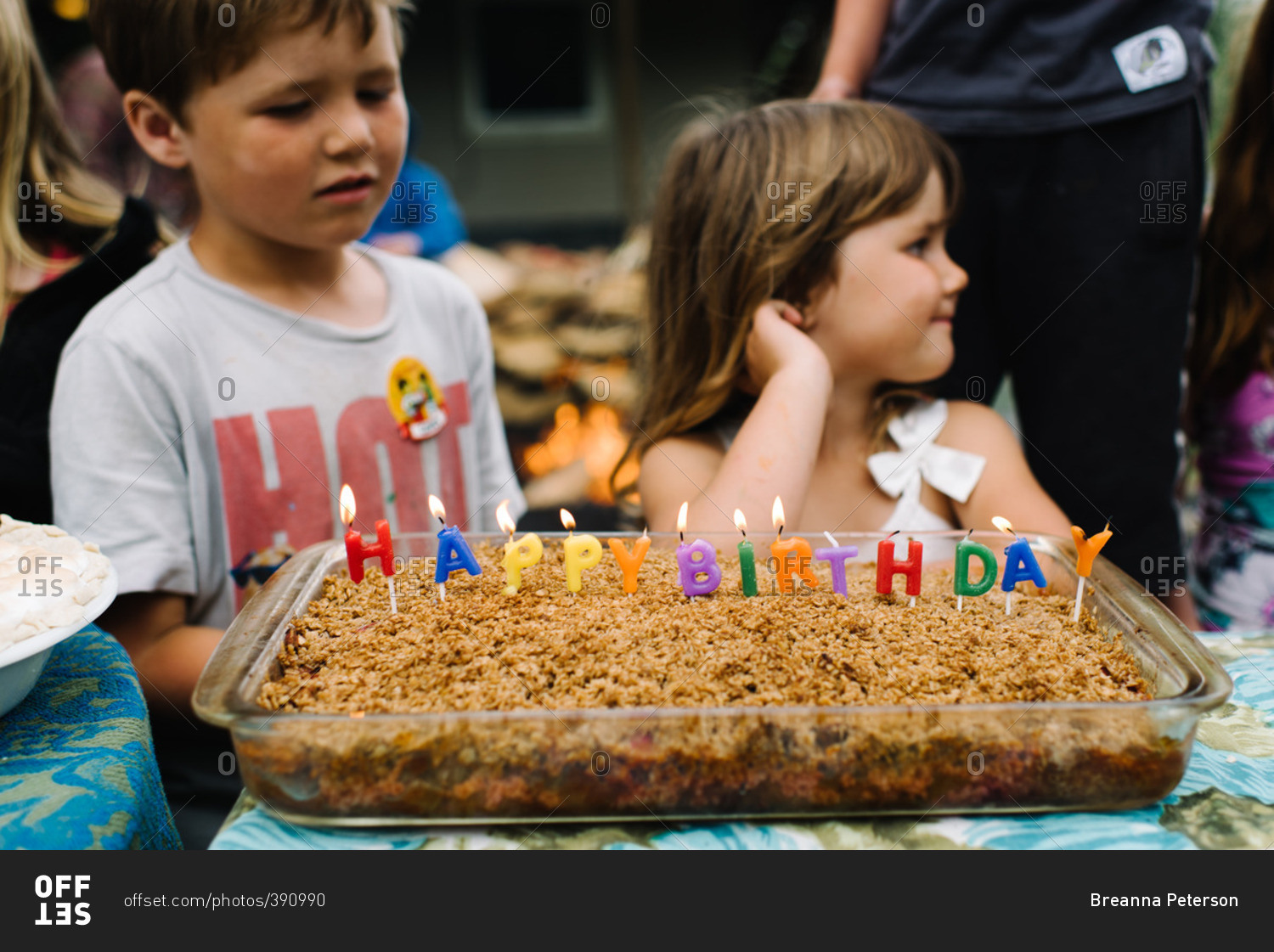 Children at a party with a cake that has happy birthday spelled out in candles