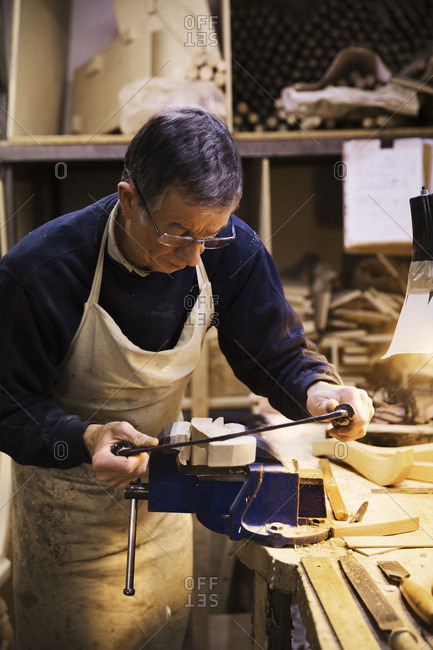 Man standing at a work bench in a carpentry workshop, working on a piece of wood secured in a bench vice