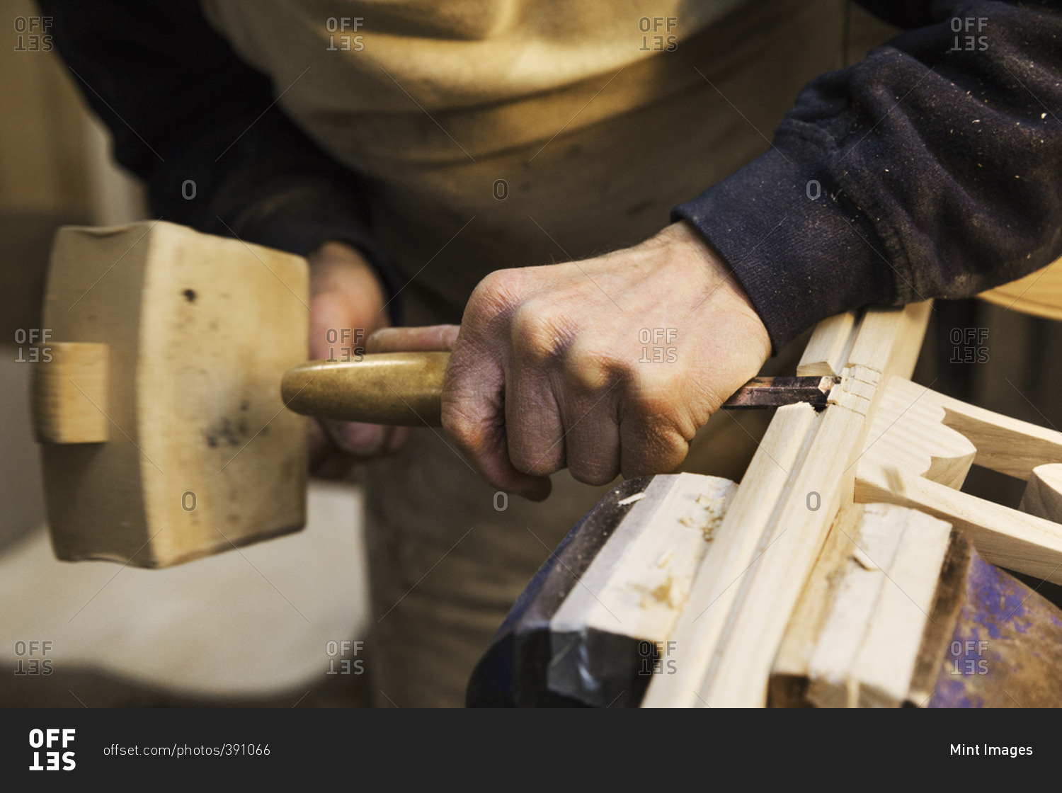 Close up of a man standing at a work bench in a carpentry workshop, working on a wooden chair with a wooden mallet and chisel