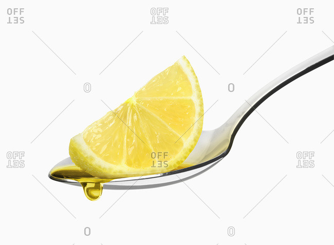 Lemon wedge on a spoon on a white background with a droplet of liquid falling from the rind