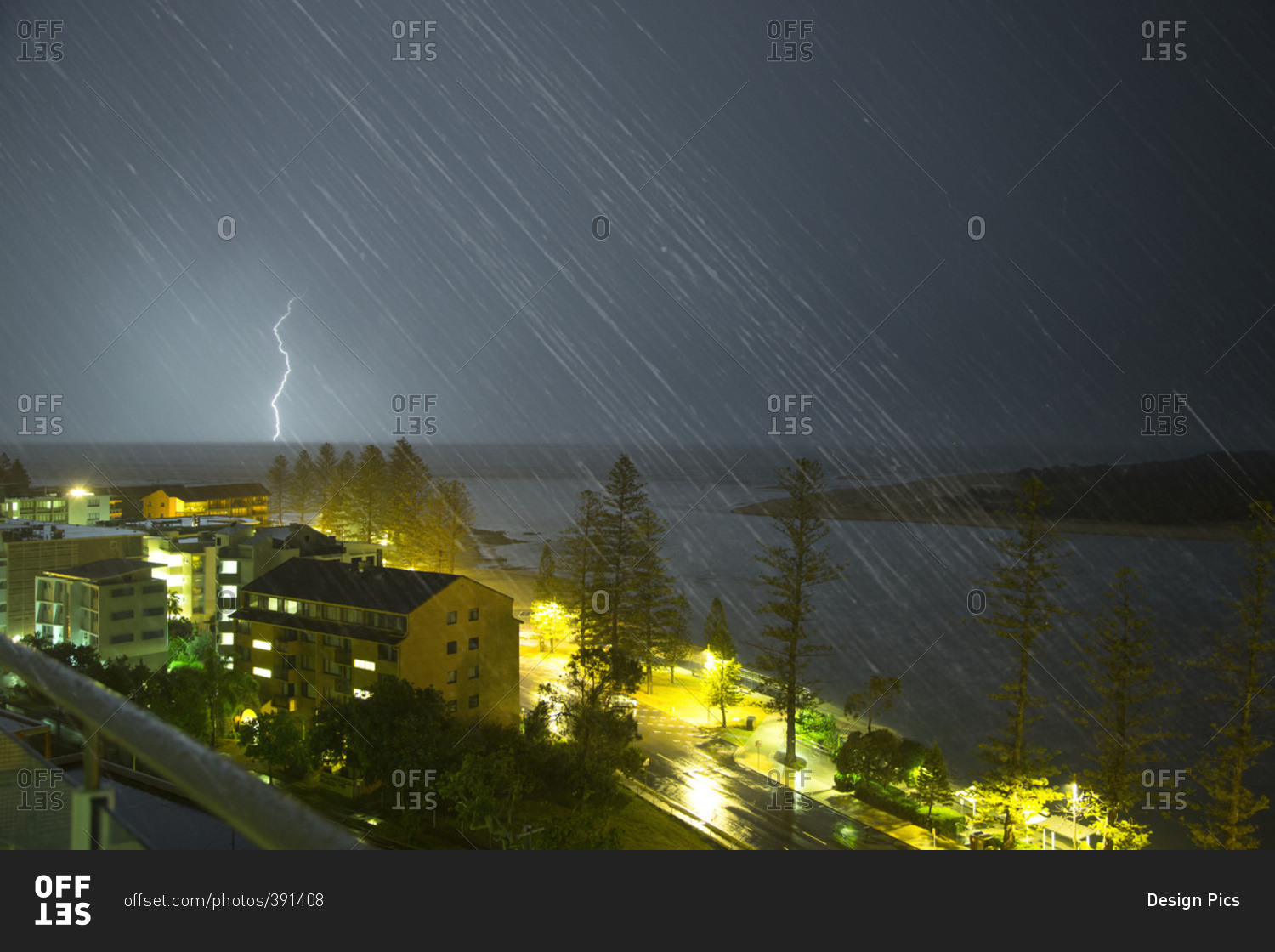 A lightning strike hits the ground in the distance and streaks of rain falling