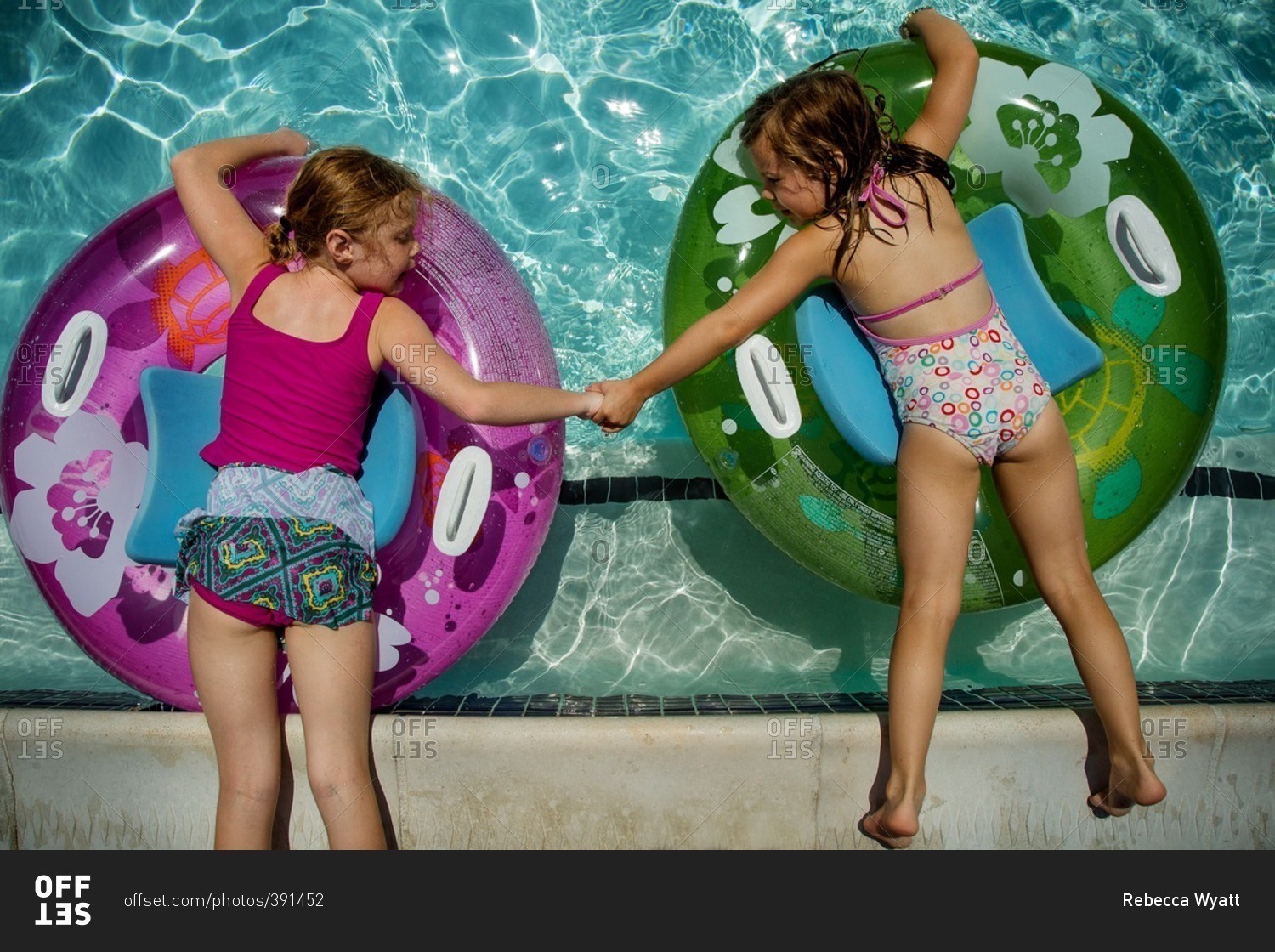 Two young girls holding hands while floating in pool stock photo OFFSET