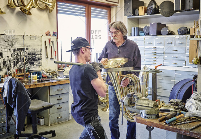 Two instrument makers repairing brass instrument in workshop